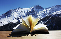 livre ouvert au premier plan, montagnes à l'arrière
