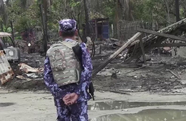 Myanmar security forces member near burnt-down houses in Rakhine State. CREDIT Steve Sandford (VOA) via <a href="https://en.wikipedia.org/wiki/2017_Rohingya_persecution_in_Myanmar#/media/File:BGP_officer_near_a_burnt_down_house_in_Rakhine_State.jpg">Wikipedia</a>