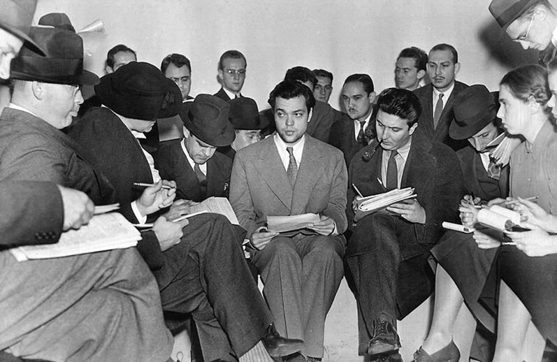 Orson Welles (center) meeting with reporters after the <i>War of the Worlds</i> radio broadcast. November, 1938. CREDIT: <a href="https://commons.wikimedia.org/wiki/File:Orson_Welles_1938_War_of_the_Worlds.jpg">The Express (Public Domain)</a>