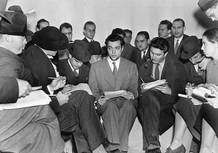 Orson Welles (center) meeting with reporters after the <i>War of the Worlds</i> radio broadcast. November, 1938. CREDIT: <a href="https://commons.wikimedia.org/wiki/File:Orson_Welles_1938_War_of_the_Worlds.jpg">The Express (Public Domain)</a>